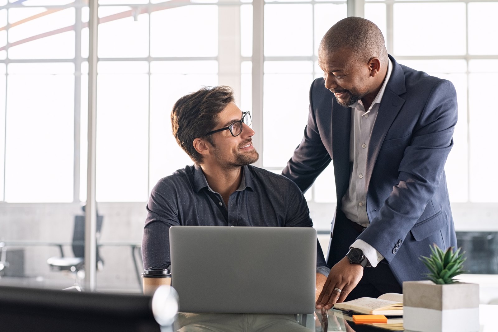 Two colleagues at a laptop, one explaining something to the other