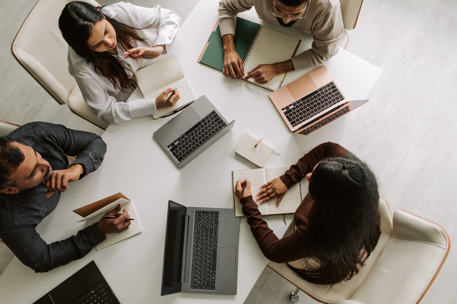 Four colleagues around a table with laptops and notebooks, working through a problem together