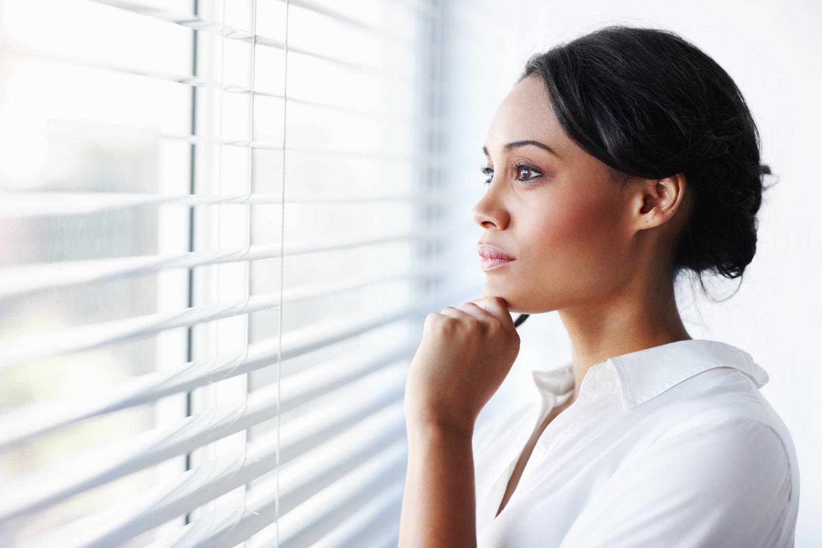 A professional woman looking out of an office window, thinking